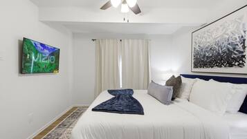 Una habitación de hotel con una cama, un ventilador de techo, un televisor en la pared y un cuadro abstracto grande.