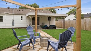 A backyard patio with Adirondack chairs, a metal grill, and a pergola with string lights. - Cozy 3BR Near AT&T Stadium w Firepit near Downtown (Arlington)
