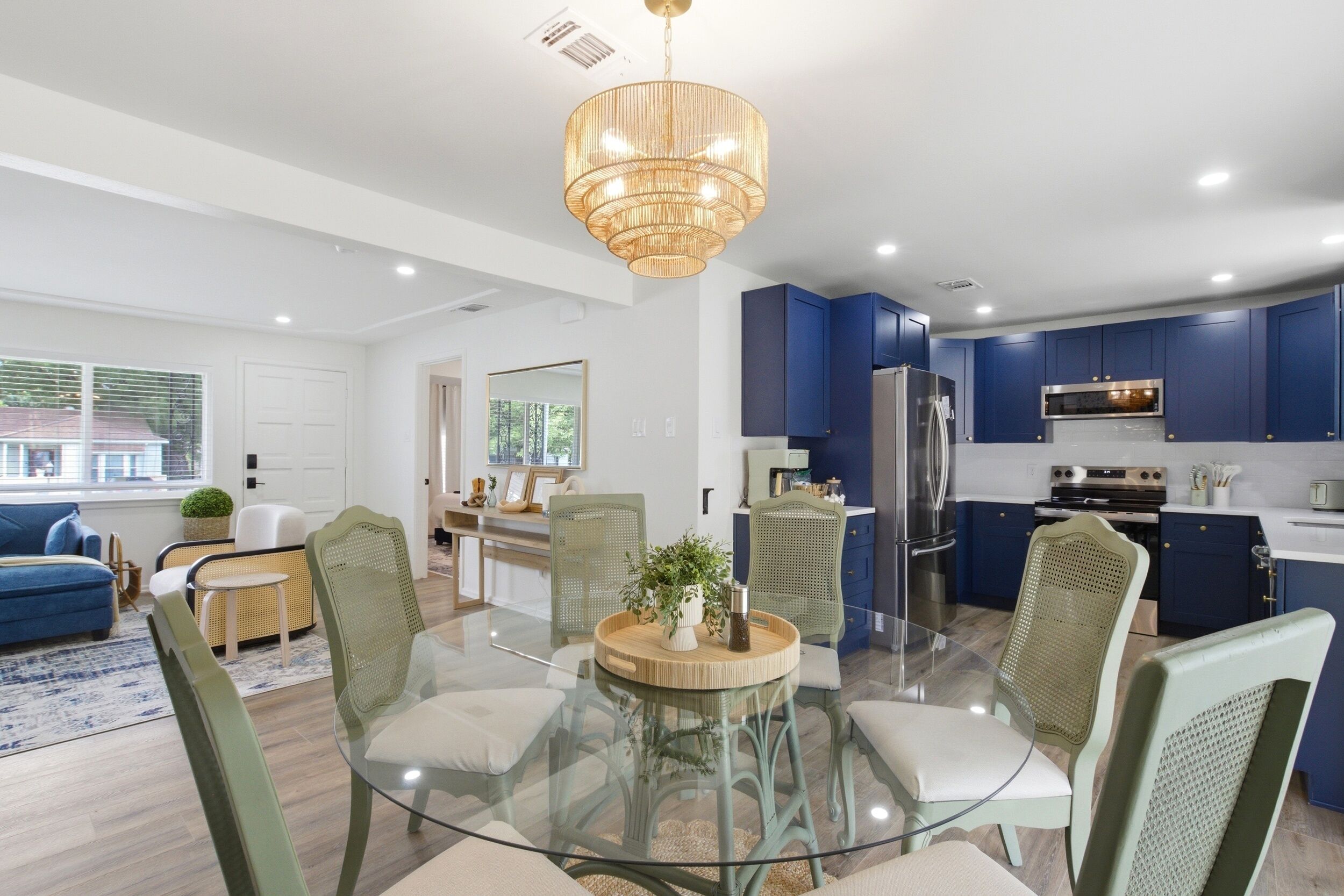 A modern kitchen with blue cabinets, stainless steel appliances, and a glass dining table with chairs.