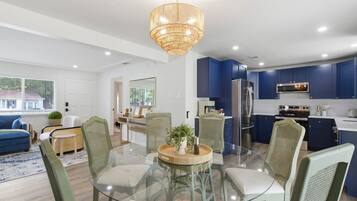 A modern kitchen with blue cabinets, stainless steel appliances, and a glass dining table with chairs.