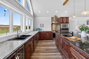 Une cuisine moderne dotée d’un grand îlot central, d’un four encastré et offrant une vue sur l’extérieur.