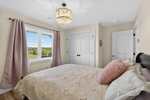 A bedroom with a bed, curtains, a chandelier, and a view of the outdoors. - SaltWind Retreat | Bay Views Near Cavendish (Kensington)