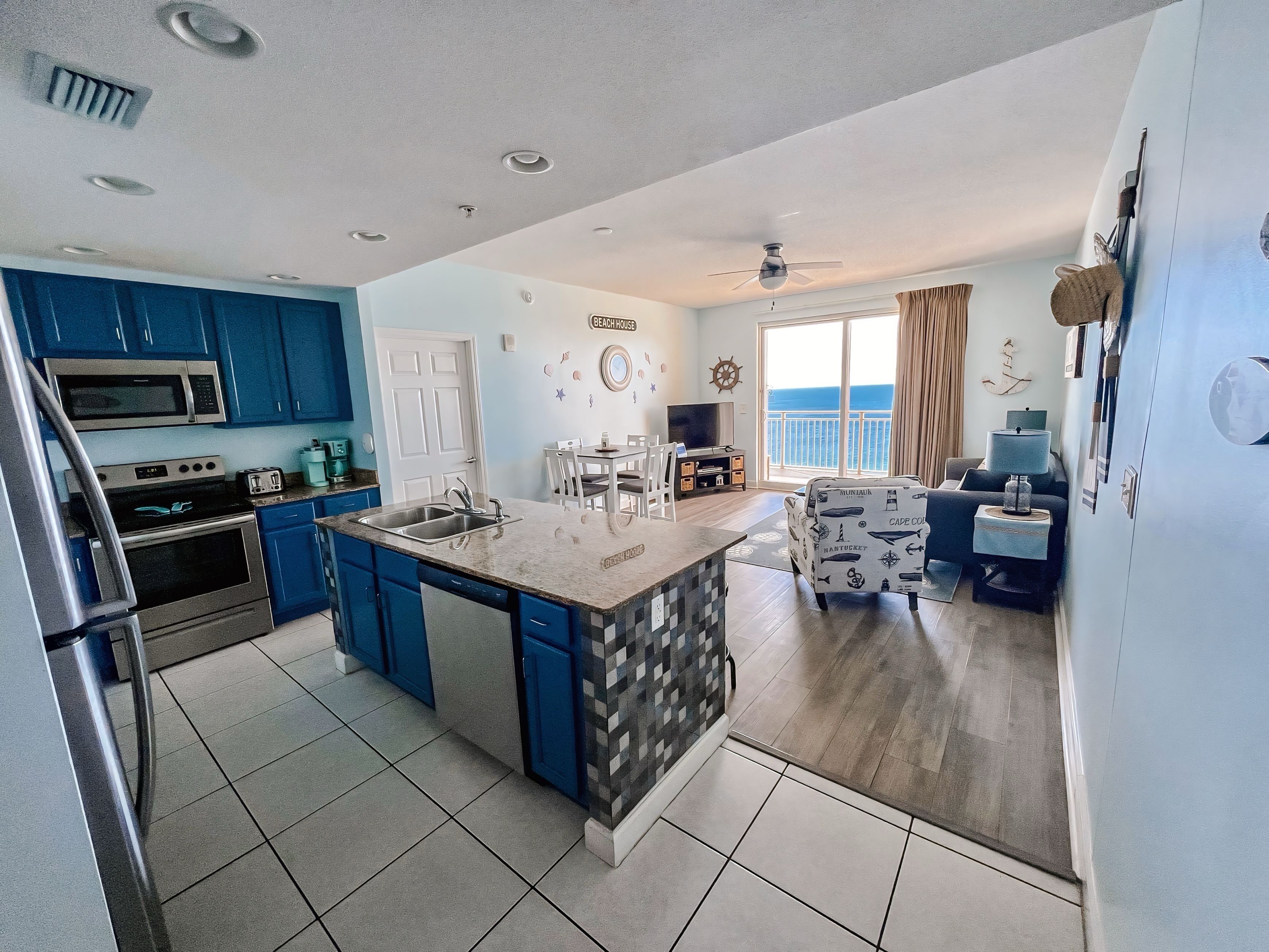Una cocina moderna con armarios azules, una isla central y un comedor con vistas al mar.
