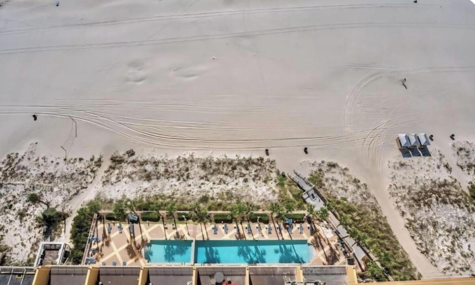 Oversigtsbillede af en strandresort med swimmingpool, strandparasoller og nogle få personer, der går på sandet.