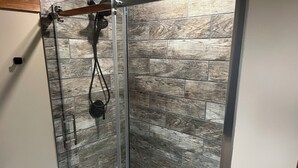 A glass-enclosed shower with a wooden-textured wall and a metal handle.
