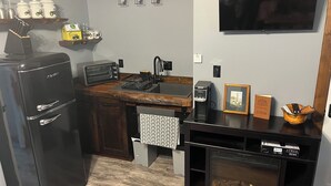 A compact kitchen with a refrigerator, toaster, sink, and a flat-screen TV mounted on the wall.