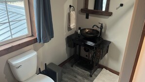A bathroom with a toilet, a sink with a basin, a mirror, and a window with curtains.