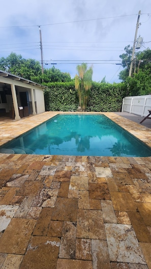 A rectangular swimming pool with a tiled deck in front.
