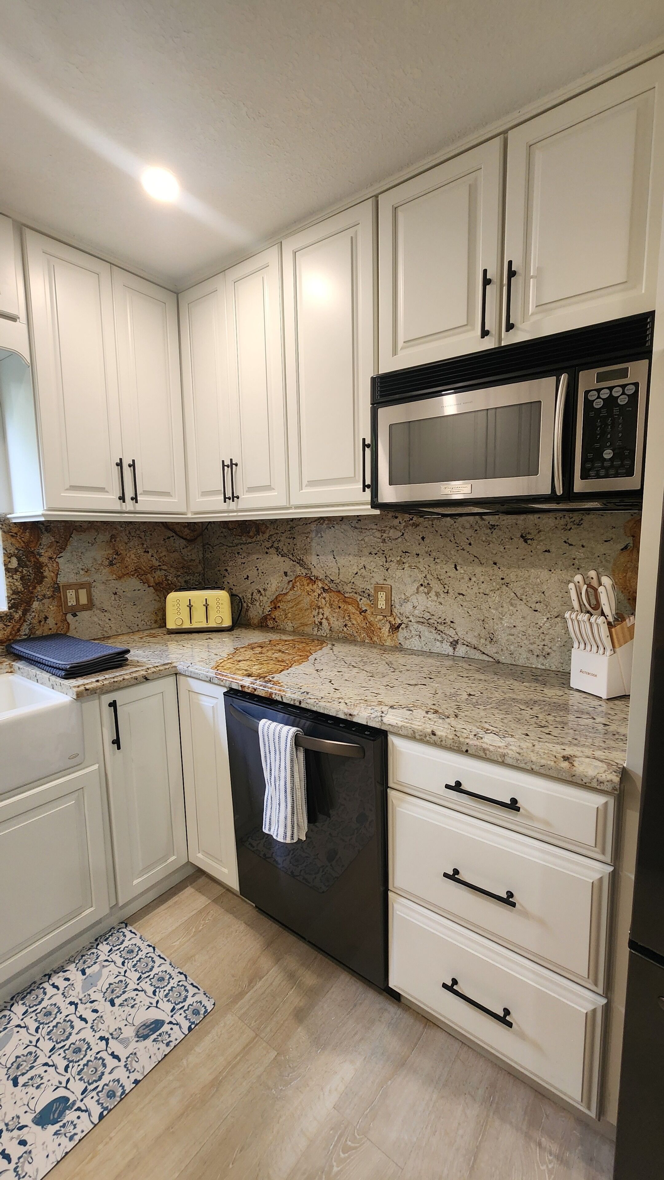 A kitchen with white cabinets, a stainless steel microwave, a toaster, and a dishwasher.