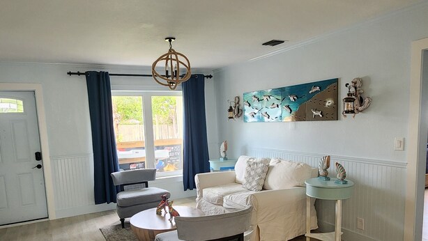 A spacious living room with a light-colored wooden floor, a white sofa, a round coffee table, and a chandelier.
