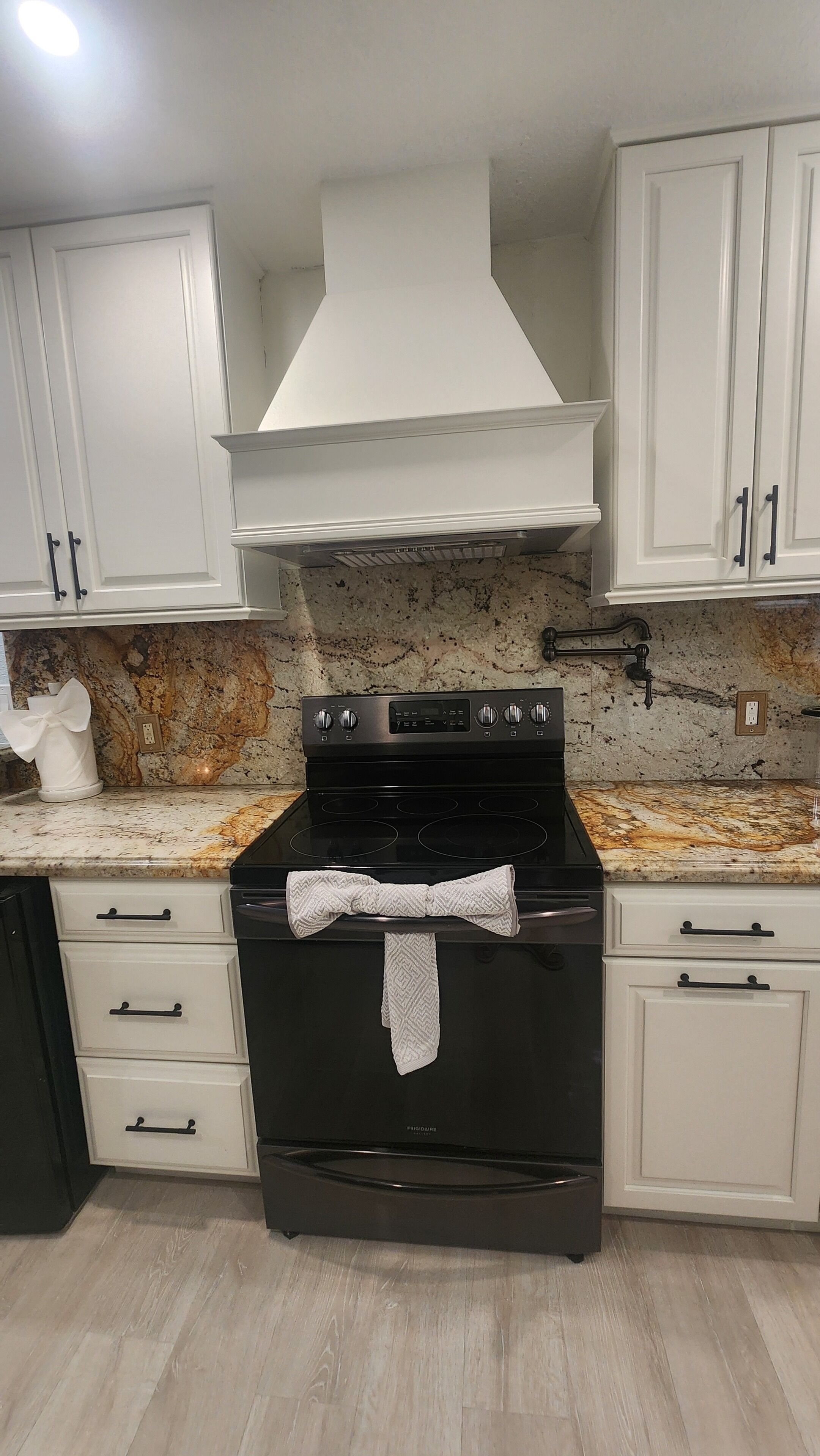 A kitchen with white cabinets, a black stove, and a marble countertop.