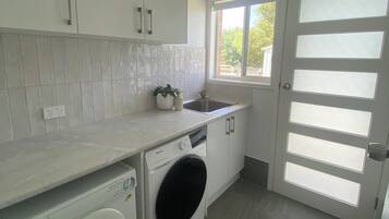 Cozinha moderna com armários brancos, máquina de lavar embutida e janela que proporciona iluminação natural.