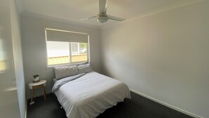 A bedroom with a bed, a ceiling fan, a window, and a small bedside table. -     Your Home Away From Home (Inverell)