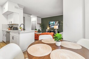 Eine moderne Küche mit weißen Schränken, einem eingebauten Backofen und einem Essbereich mit einem Holztisch und gewebten Platzsets.