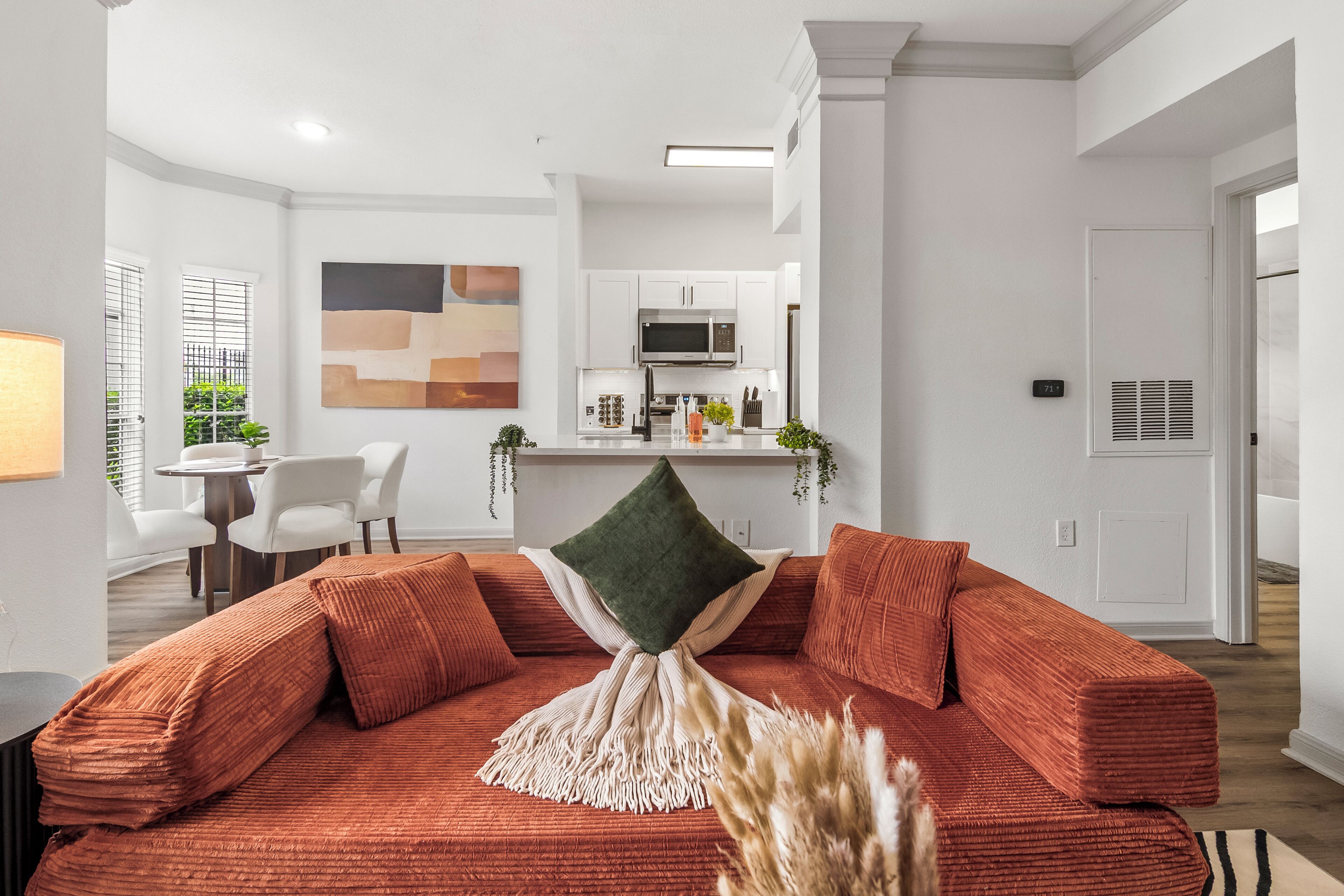A modern living room with a sofa, a dining area with chairs, and a kitchen with appliances.