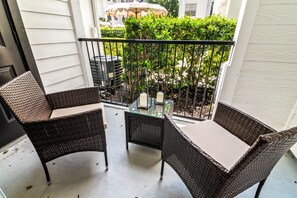 A balcony with two wicker chairs and a glass table, overlooking a garden with a white building in the background. - Modern River Oaks Retreat / FIFA + Pool & Gym (Houston)