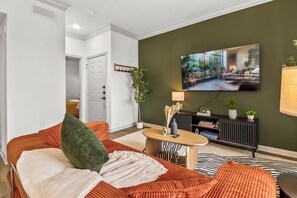 A modern living room with a sofa, a coffee table, and a television mounted on the wall. - Modern River Oaks Retreat / FIFA + Pool & Gym (Houston)