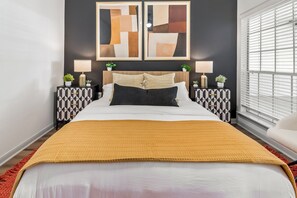 A bedroom with a bed, two bedside tables, a headboard, and a window with blinds.