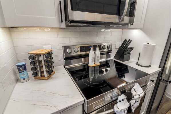 A modern kitchen with stainless steel appliances, a wooden spice rack, and a microwave above the stove.