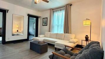 Ein modernes Wohnzimmer mit Deckenventilator, einer Couch, einem Sessel und einer Lampe.