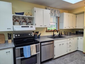 A modern kitchen with white cabinets, stainless steel appliances, and a window with a floral valance.