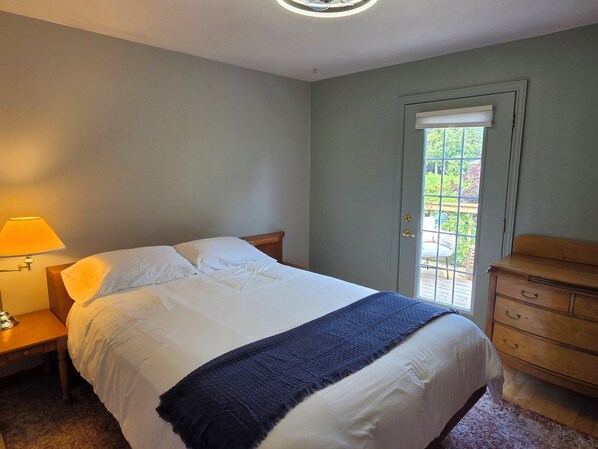 A bedroom with a bed, a nightstand, a dresser, and a door leading to an outdoor area.