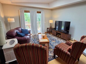 A living room with a leather sofa, striped armchairs, a coffee table, a television, and a speaker.