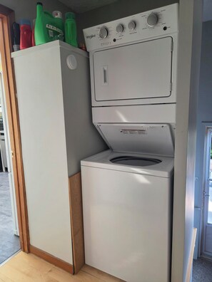 A compact washer and dryer unit with a control panel on top, placed in a corner of a room with a wooden floor.