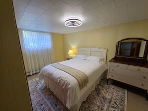 A bedroom with a bed, a bedside lamp, a dresser, a mirror, and a ceiling fan.
