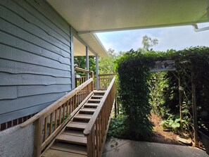 A wooden staircase leading to a covered porch with a view of a garden.
