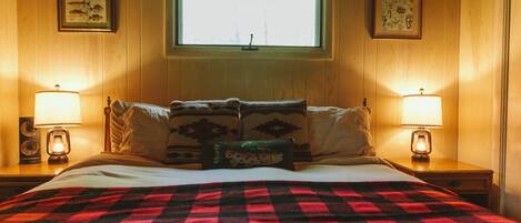 A bed with a red and black checkered blanket, two bedside lamps, and a window above.