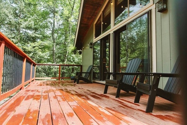 A wooden deck with chairs, large windows, and a view of a forest.