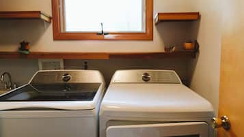Un espace buanderie comprenant deux machines à laver, une fenêtre au-dessus et une étagère en bois sur laquelle se trouve une tasse.