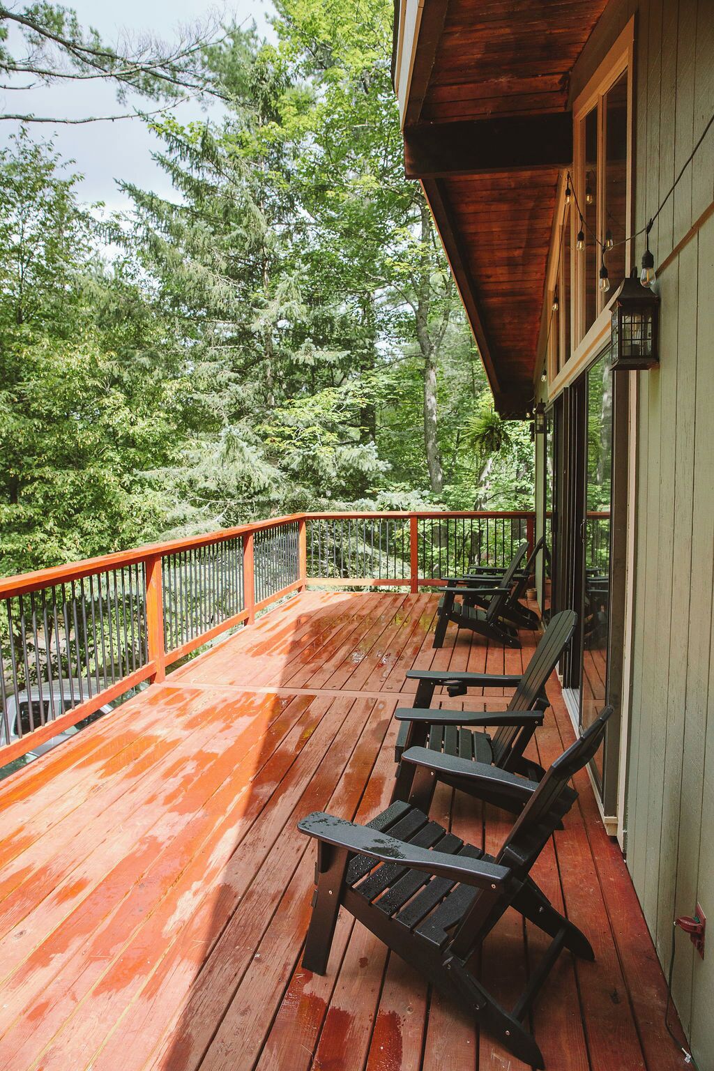 Une terrasse en bois avec une rambarde, deux fauteuils Adirondack et une vue sur une zone boisée.
