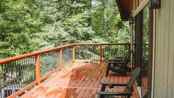 Une terrasse en bois avec une rambarde, deux fauteuils Adirondack et une vue sur une zone boisée.