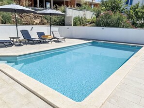 A rectangular swimming pool with clear blue water, surrounded by light-colored tiles. There are lounge chairs and umbrellas around the pool area. - Nicolina by Interhome (Poreč/Kaštelir)