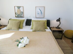 Un llit ben fet amb almoinades estampades, un arranjament floral decoratiu i dos quadres a la paret.