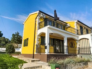 Edifici de dues plantes amb façana groga, un balcó amb barana negra i una escalinata de pedra que condueix a l'entrada.