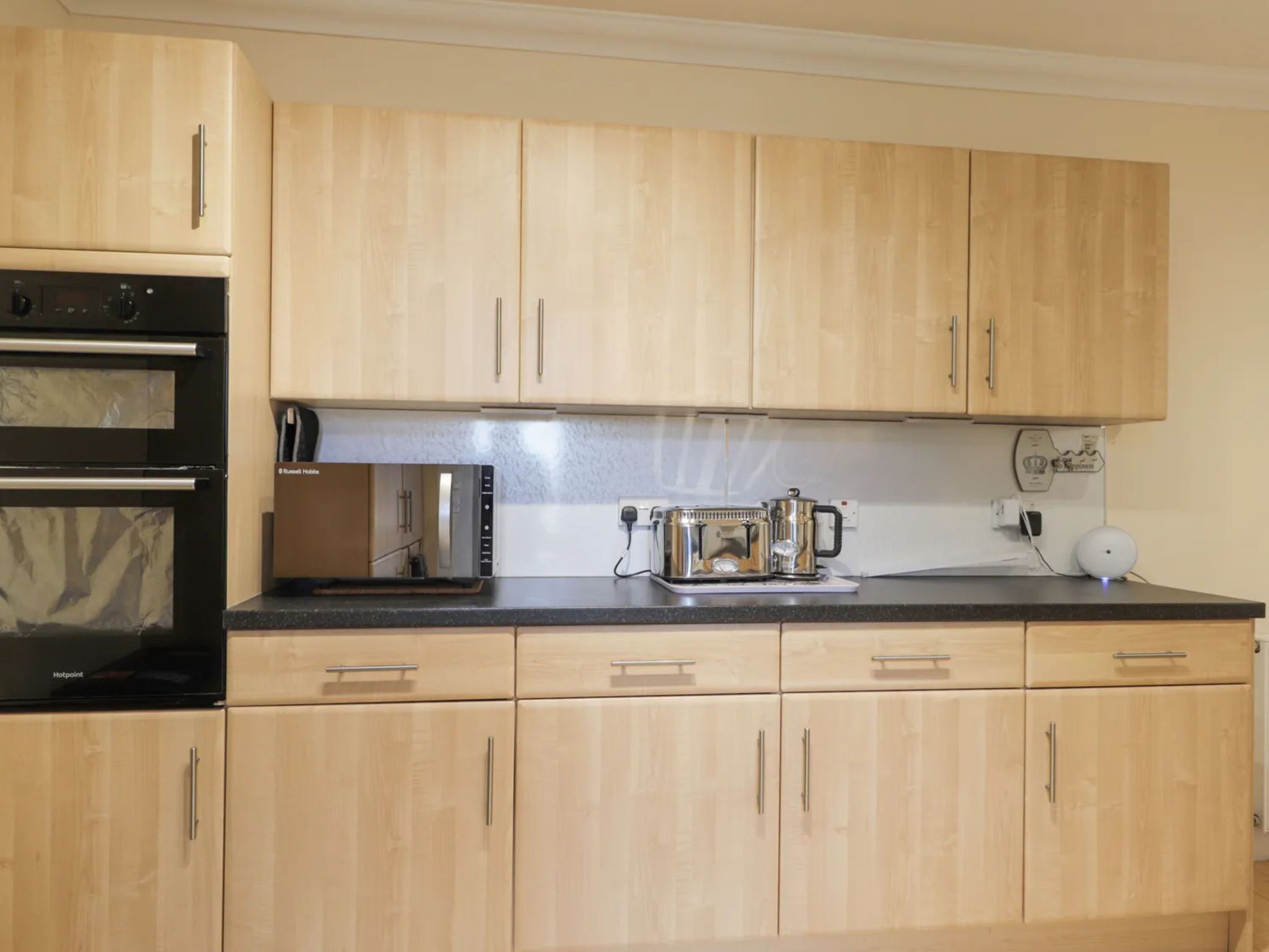 A kitchen with wooden cabinets, a built-in oven, a toaster, and a kettle on the countertop.