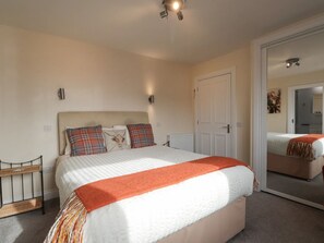A bedroom with a bed, a bedside table, a mirror, and a door leading to a bathroom. - Ballinreich by Interhome (Inverness)