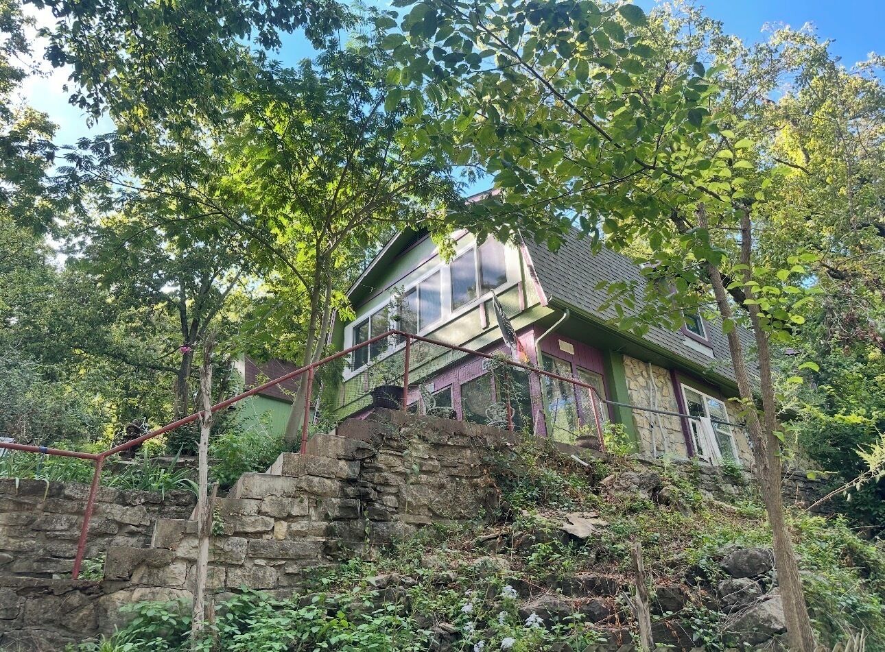 A house with a stone staircase leading up to a wooden deck, surrounded by trees.