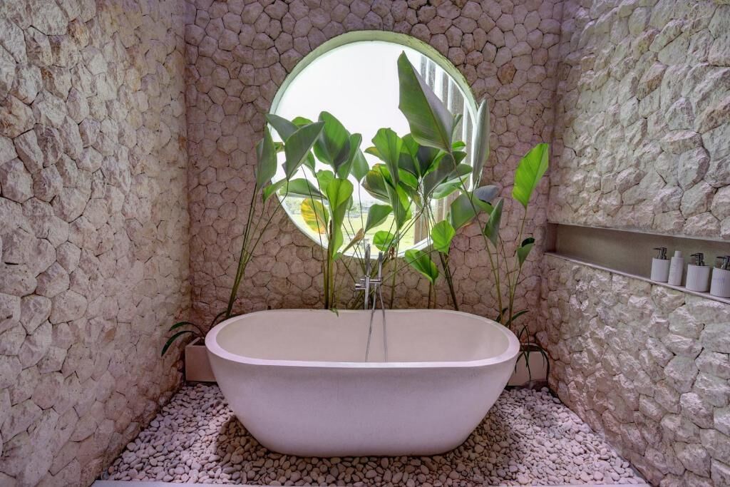 Ein Badezimmer mit einer freistehenden Badewanne, einer Steinwand und einem Fenster mit Pflanzen.