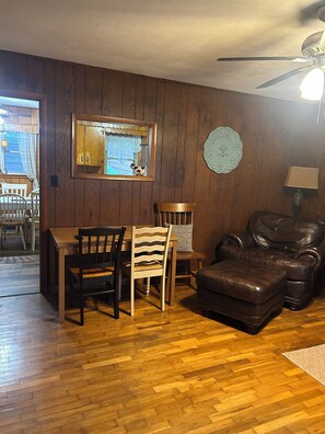 A dining area with a wooden table and chairs, a leather armchair, a clock, and a ceiling fan.