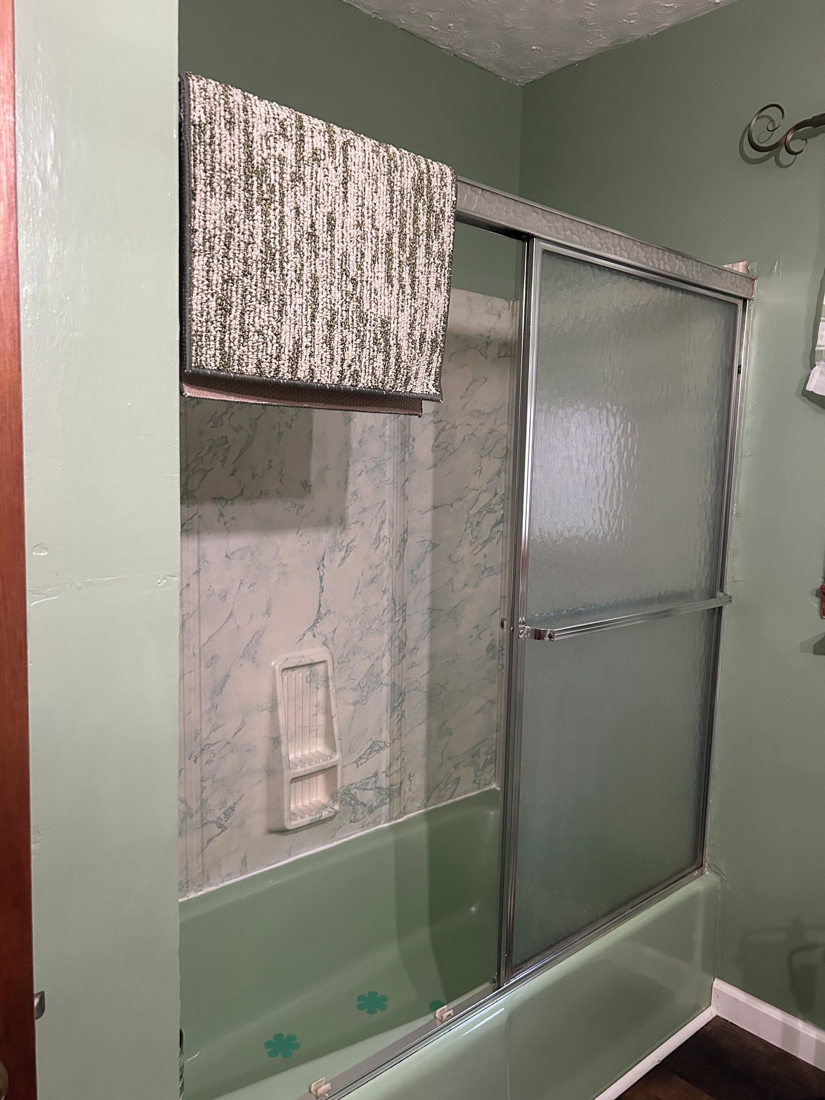 A bathroom with a glass shower enclosure, a marble-patterned wall, and a towel rack.