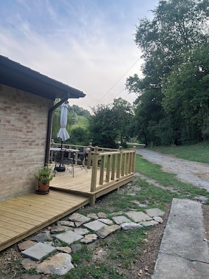 A wooden deck with a brick wall, a potted plant, outdoor furniture, and a stone pathway. - Whispering Willow Ranch House near Ethridge-home of the Amish Community (Lynnville)