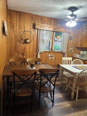 A wooden dining room with a table and chairs, a ceiling fan, and a window with curtains.