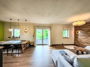 A modern living space with a dining area, a sofa, and a large window providing a view of the outdoors. - ApaLuza by Interhome (Wojcieszyce)