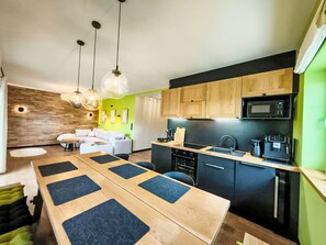 Eine moderne Küche mit Holzschränken, einer schwarzen Mikrowelle und einem Essbereich mit einem Holztisch und blauen Kissen.