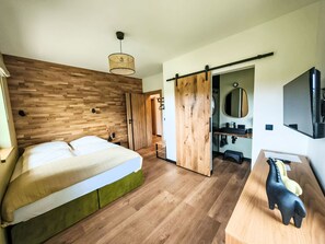 A modern bedroom with a wooden headboard, a bed with green bedding, a bedside table, a hanging light fixture, a sliding door leading to a bathroom, a mirror, and a mounted television. - ApaLuza by Interhome (Wojcieszyce)