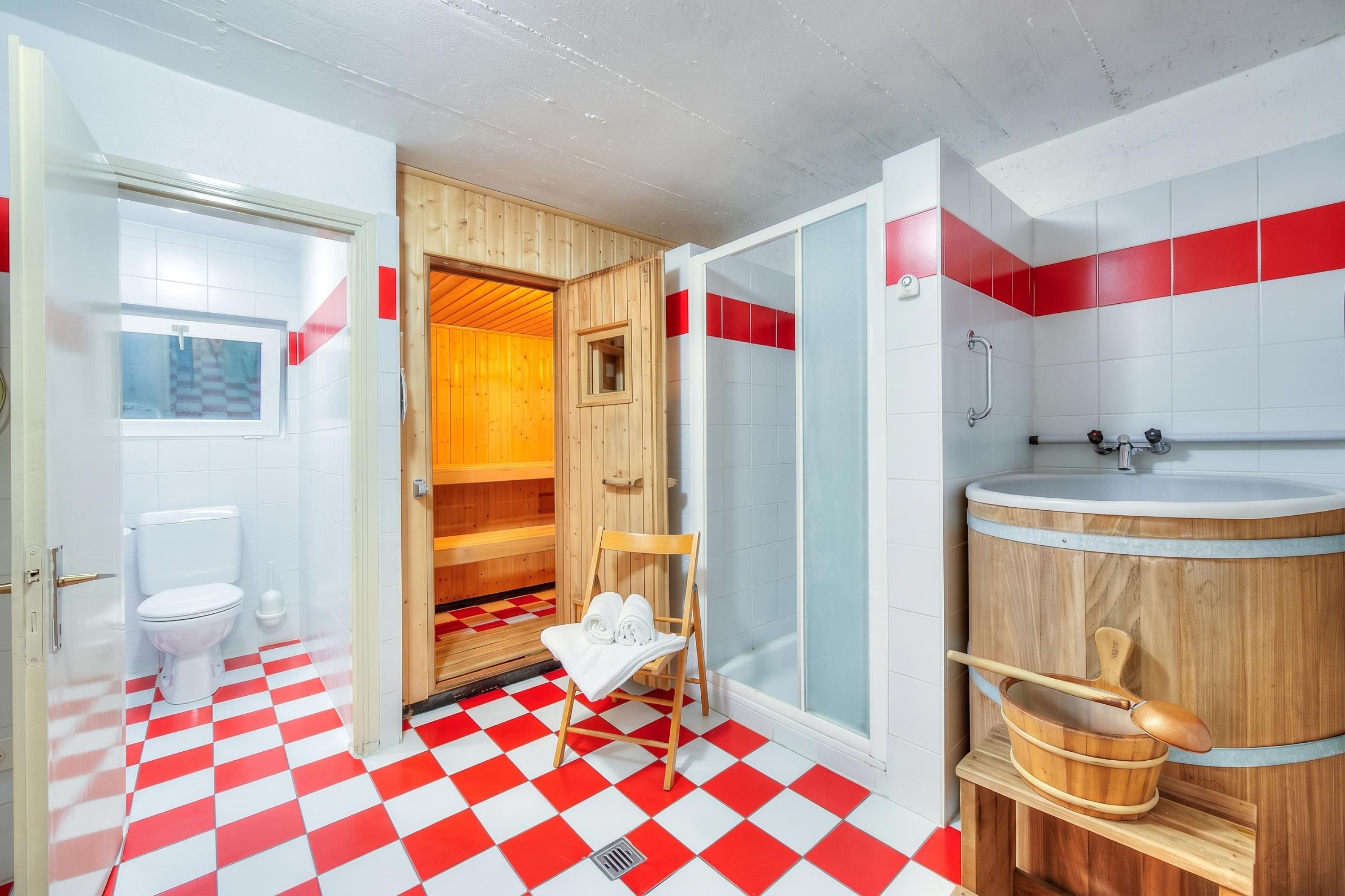 Une salle de bain avec un carrelage à motifs géométriques, un sauna en bois, un espace douche et un lavabo avec un receveur en bois.